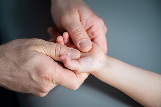 Osteopata Andrzej Szwajlik trzyma dłoń niemowlęcia, dziecka w trakiec wykonywania technik osteopatycznych w rehabilitacji ręki, dłoni.