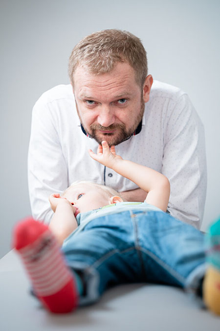 Leżące na kozetce dziecko łapie za brodę osteopatę Andrzeja Szwajlik.